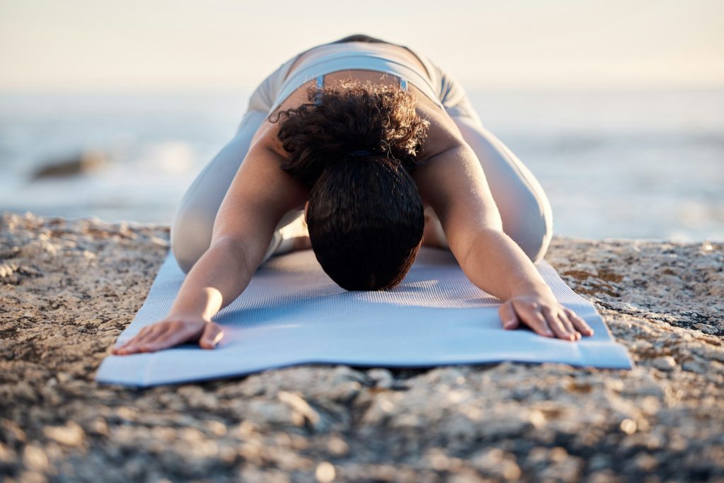 Yoga, meditate and fitness with a woman on a rock at the beach for mental health, wellness or exerc